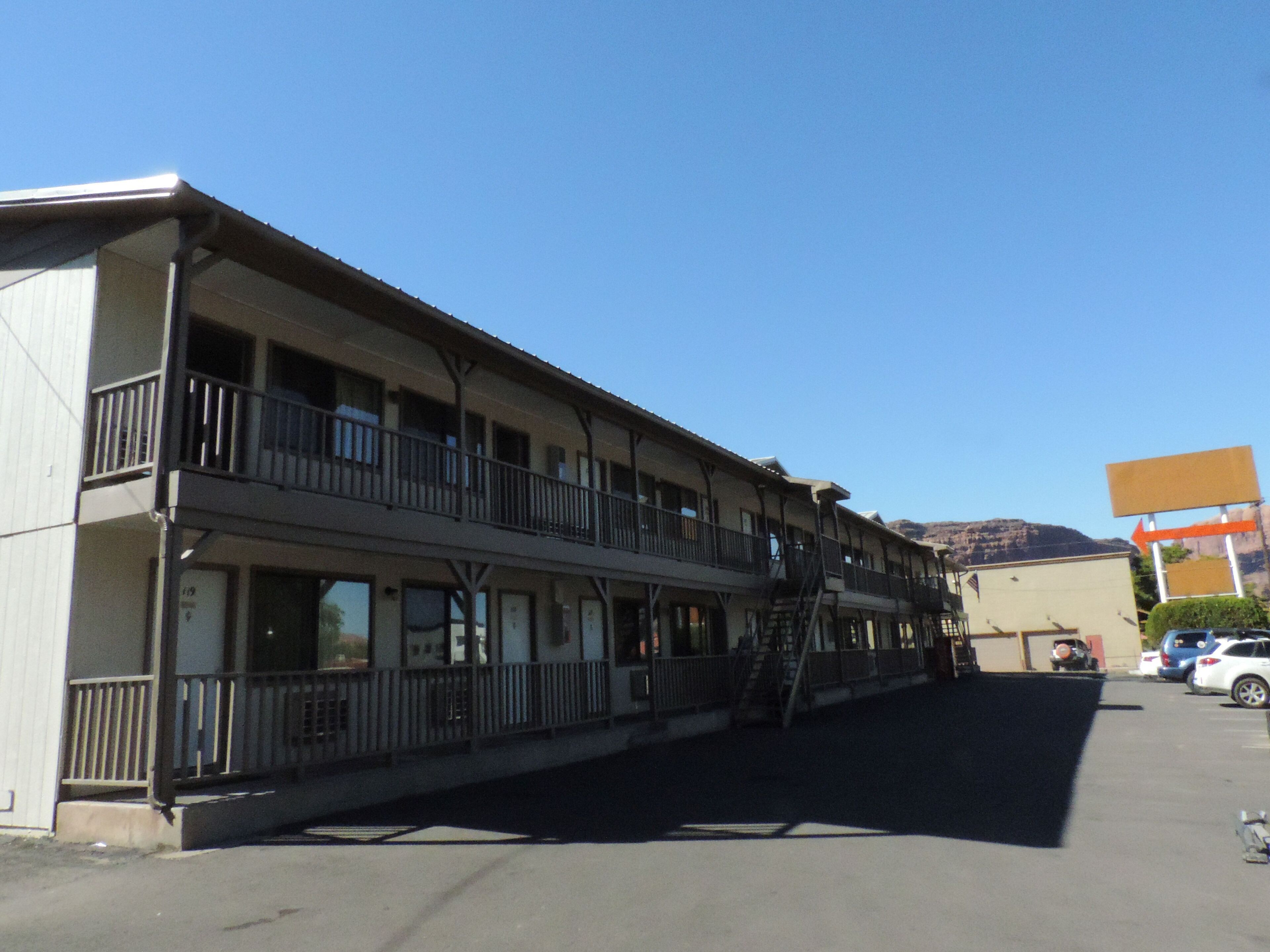 Un motel à deux étages, doté de balcons, d’un parking et avec une montagne en toile de fond.