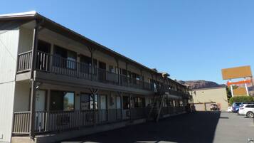 A two-story motel with balconies, a parking lot, and a mountain in the background.