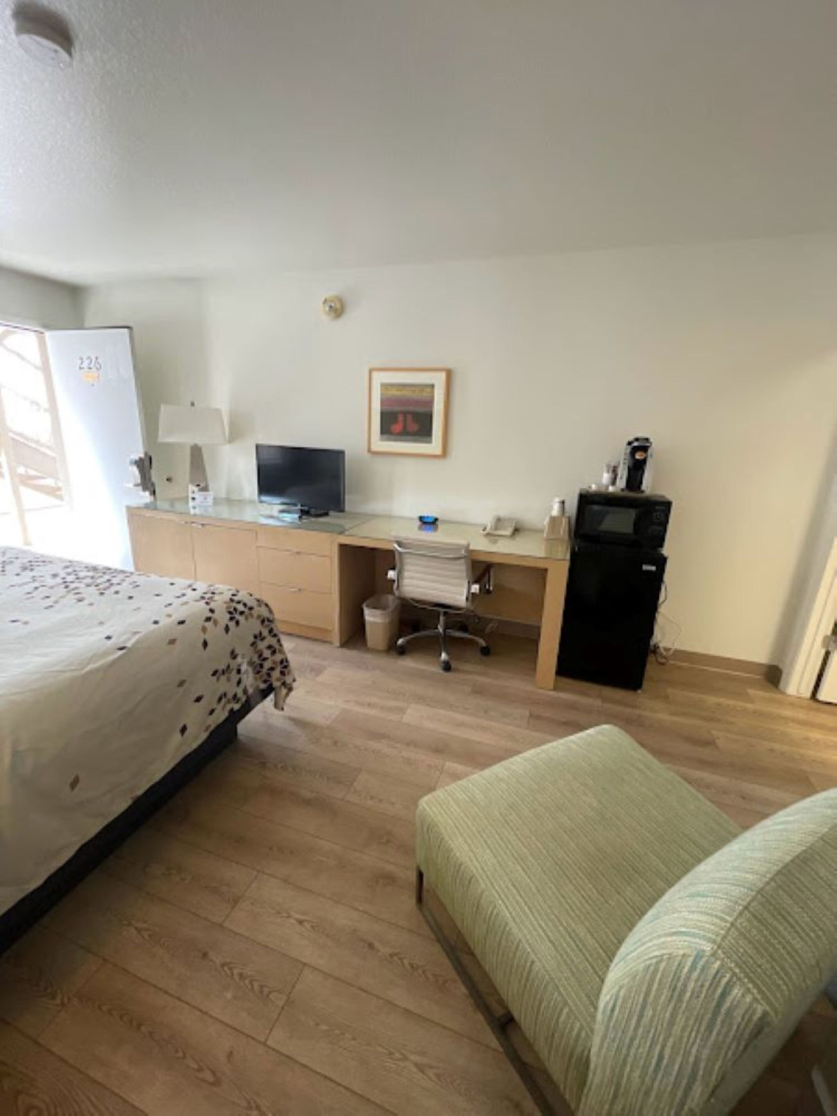 Quarto de hotel com cama, escrivaninha, cadeira, televisão, frigorífico e micro-ondas.