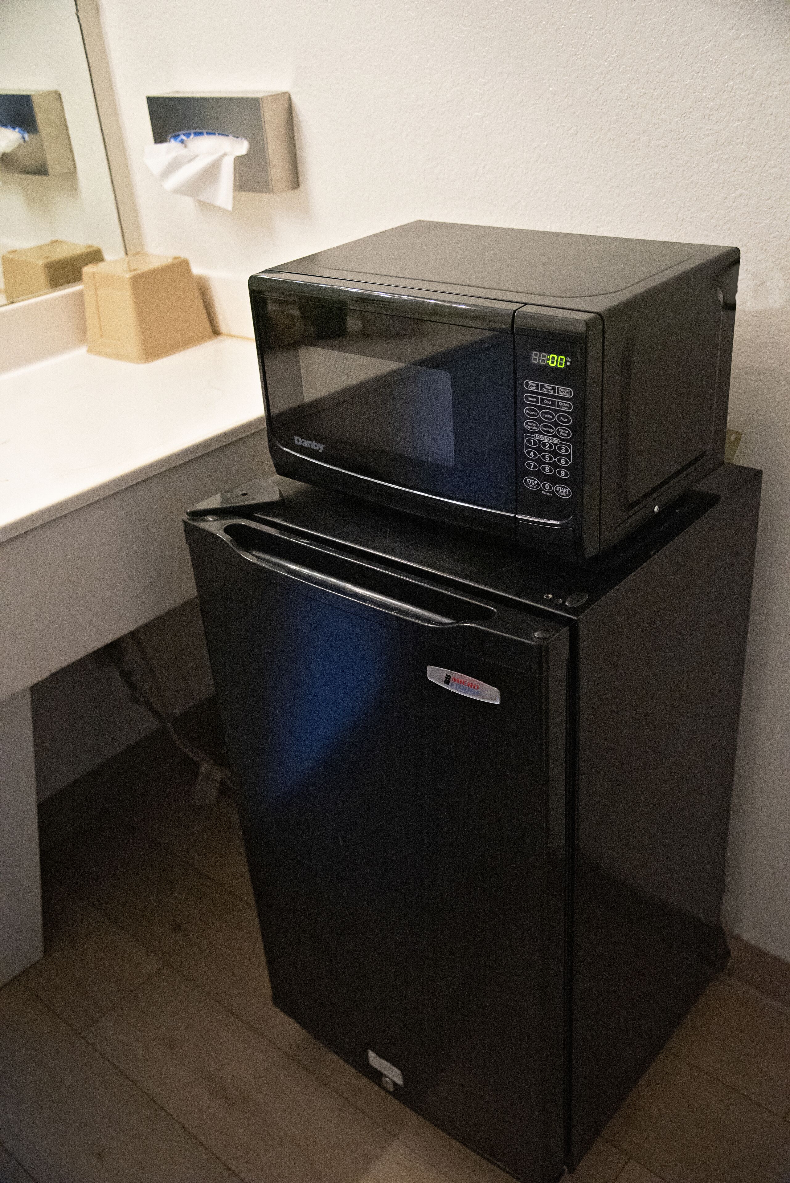 Un refrigerador negro compacto y un microondas integrados en una pequeña cocina.
