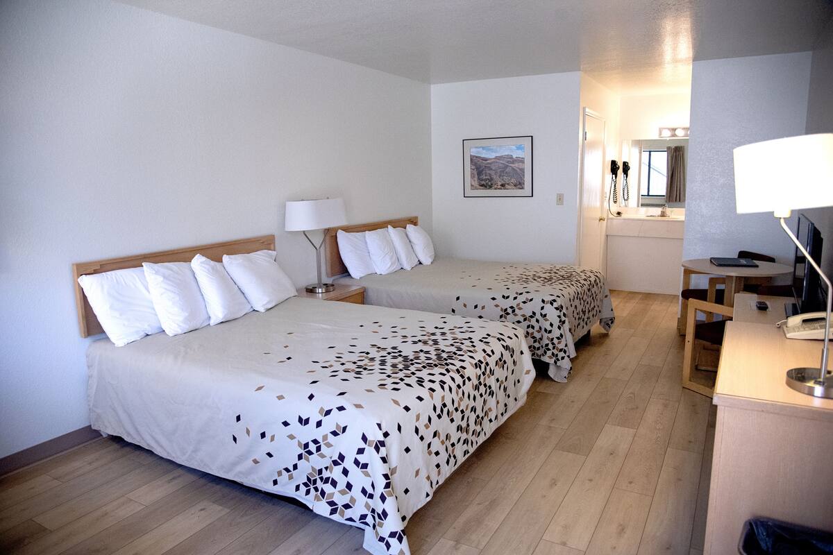 A hotel room with two beds, a desk, a chair, a lamp, a phone, and a picture on the wall.