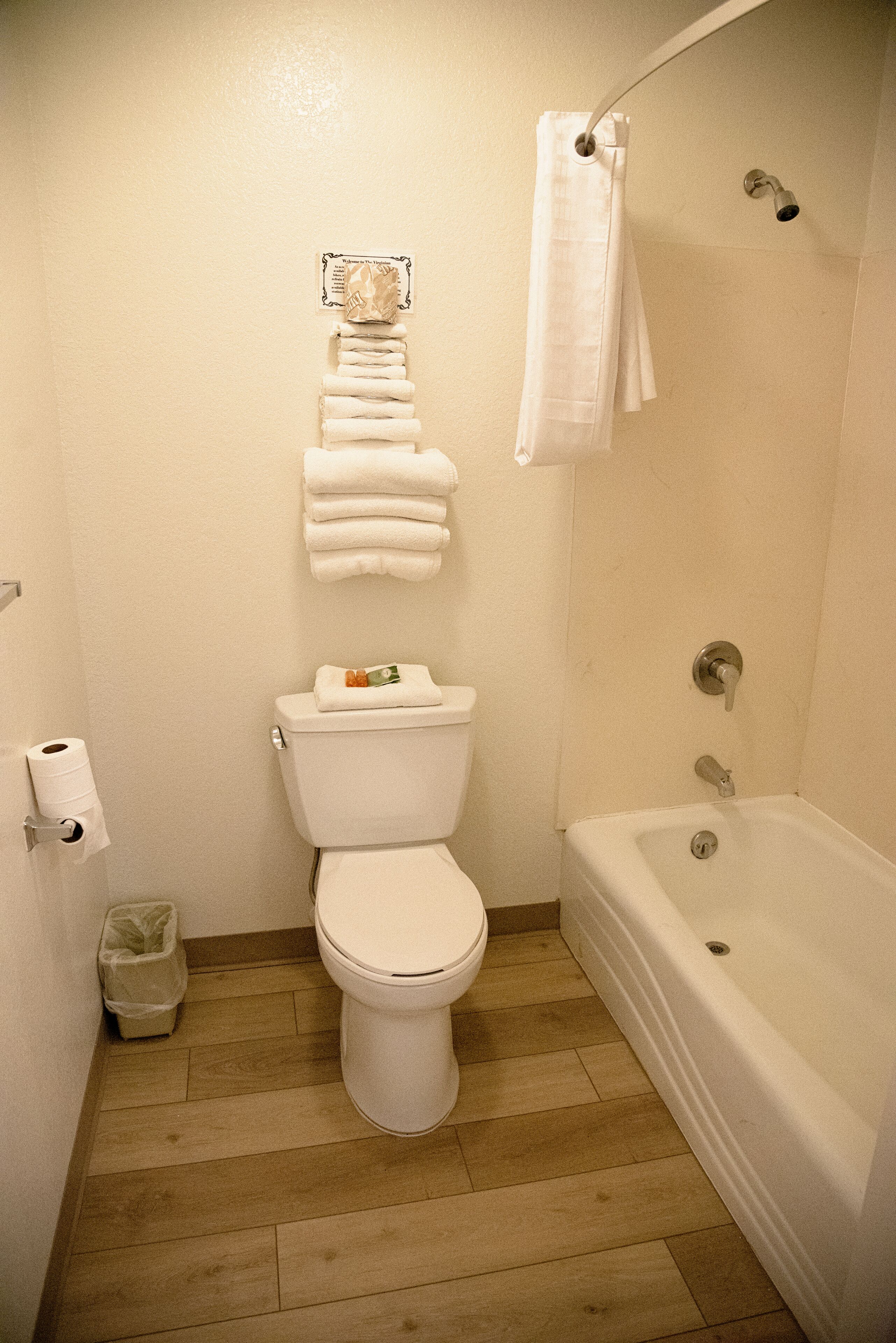 A bathroom with a toilet, a stack of white towels, a shower curtain, and a bathtub.