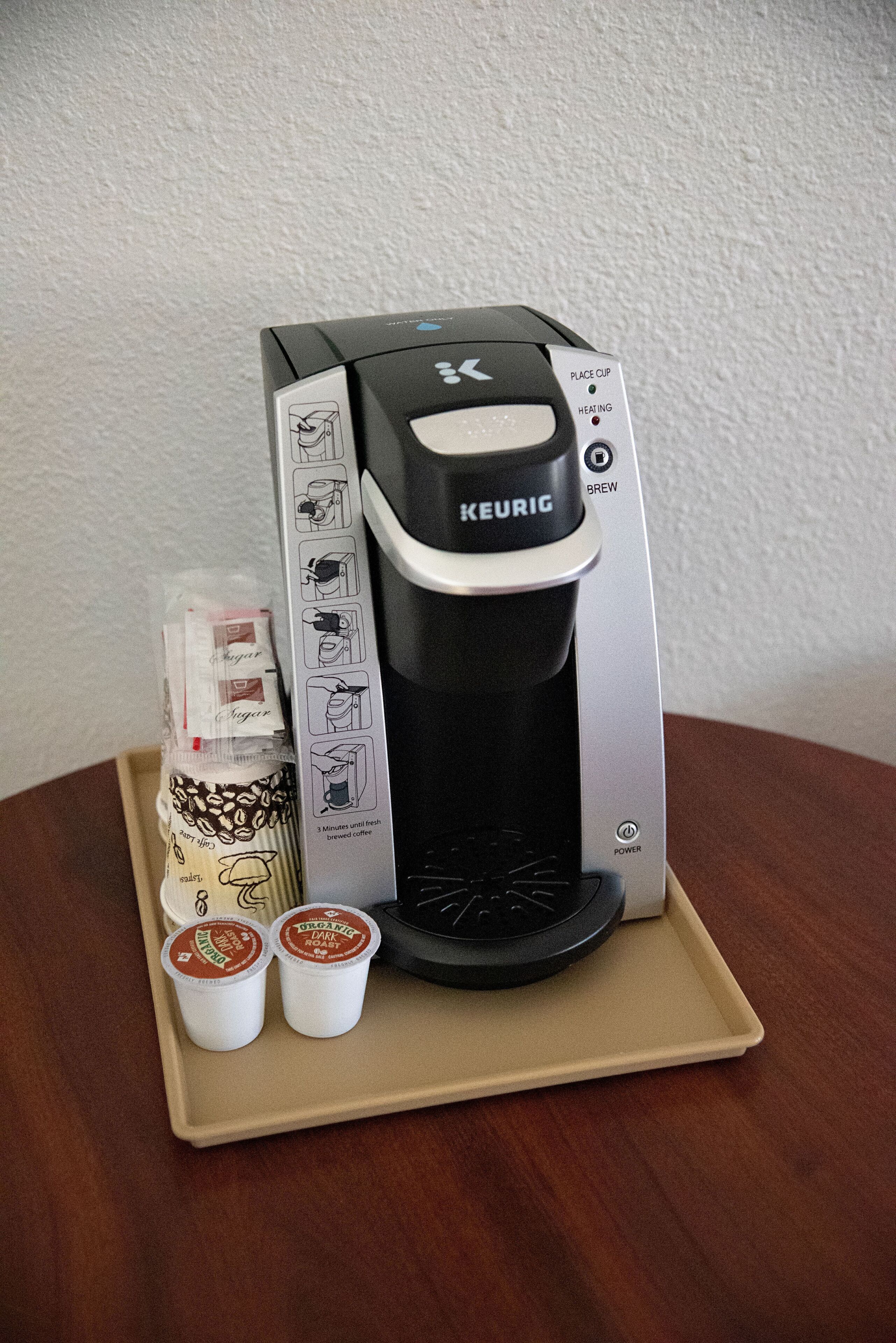 A Keurig coffee maker with a tray containing two disposable coffee cups and a coffee pod.