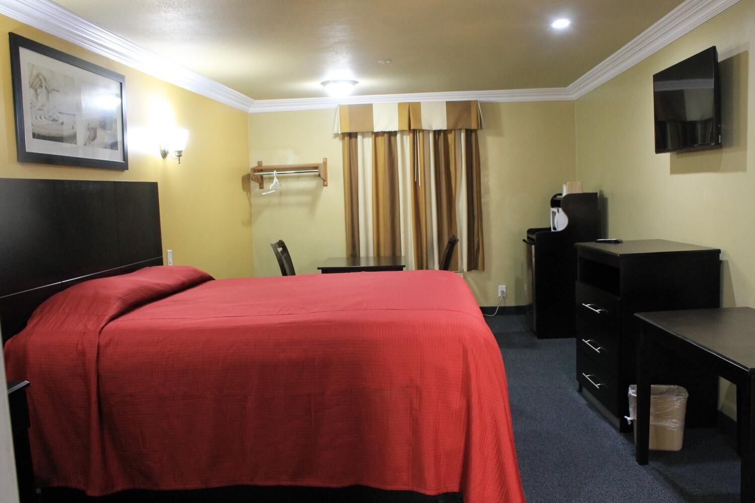 Habitación de hotel con cama, escritorio, silla, televisión y ventana con cortinas.