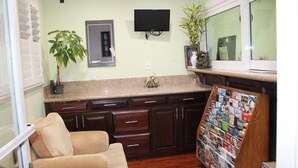 A kitchen with dark wooden cabinets, a granite countertop, a television mounted above the cabinets, a potted plant, and a bulletin board with various items pinned to it. - El Rancho Inn Hawthorne (Hawthorne)