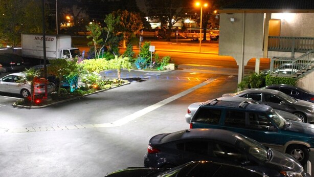 A parking lot with several cars and a truck, surrounded by greenery and illuminated by streetlights. - El Rancho Inn Hawthorne (Hawthorne)