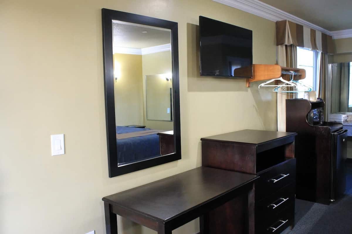 Quarto de hotel com cama, um espelho grande, TV de tela plana, cômoda com gavetas e um porta-roupas com cabides.