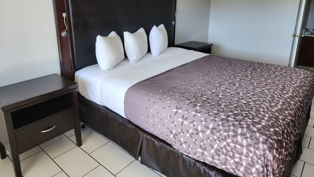 A neatly made bed with a patterned bedspread, a dark headboard, and white pillows. - Pacific Inn (Crescent City)