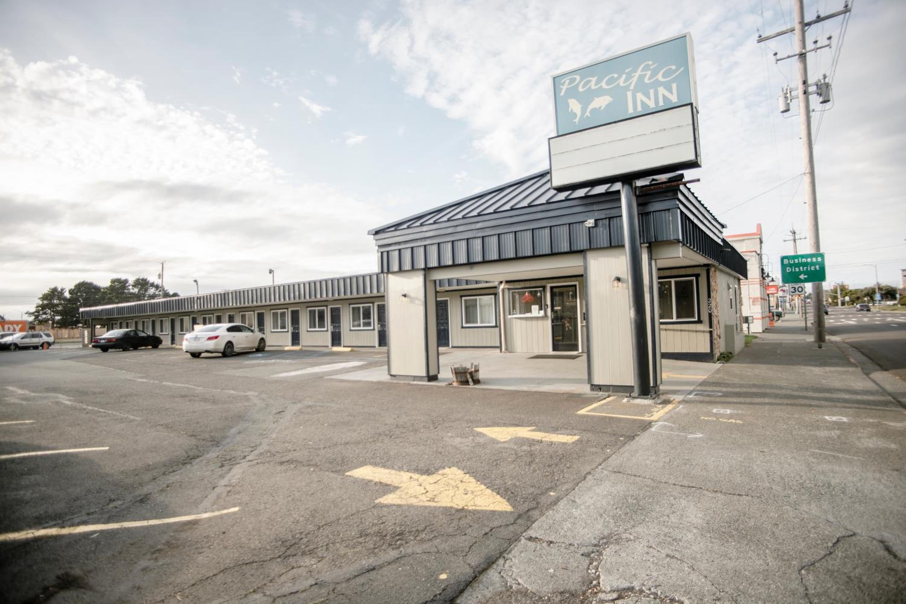 A Pacific Inn building with a signboard, parking lot, and directional arrows on the pavement.