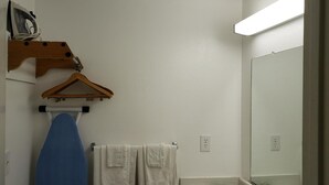 A bathroom with a hanging clothes rack, a blue ironing board, and a white towel. - Pacific Inn (Crescent City)
