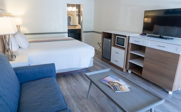 A hotel room with a bed, a desk with a TV, a small fridge, and a sofa.