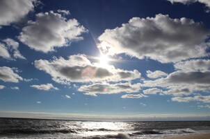 A beach with the sun shining through scattered clouds.