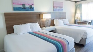 A hotel room with two beds, a nightstand with a lamp, a desk with a chair, and artwork on the walls. - Admiral on Baltimore (Rehoboth Beach)