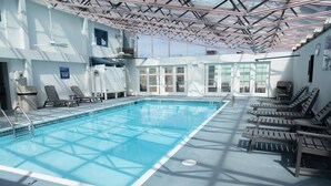 An indoor swimming pool with clear blue water, surrounded by lounge chairs and a ceiling with a geometric pattern. - Admiral on Baltimore (Rehoboth Beach)