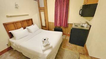 Habitación de hotel con cama, kitchenette pequeña, espejo, ventana con cortina y televisor montado en la pared.