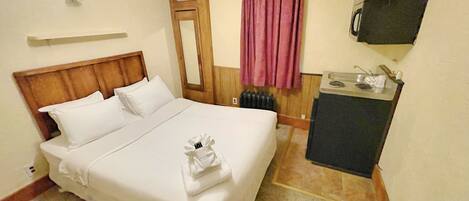 Habitación de hotel con cama, kitchenette pequeña, espejo, ventana con cortina y televisor montado en la pared.