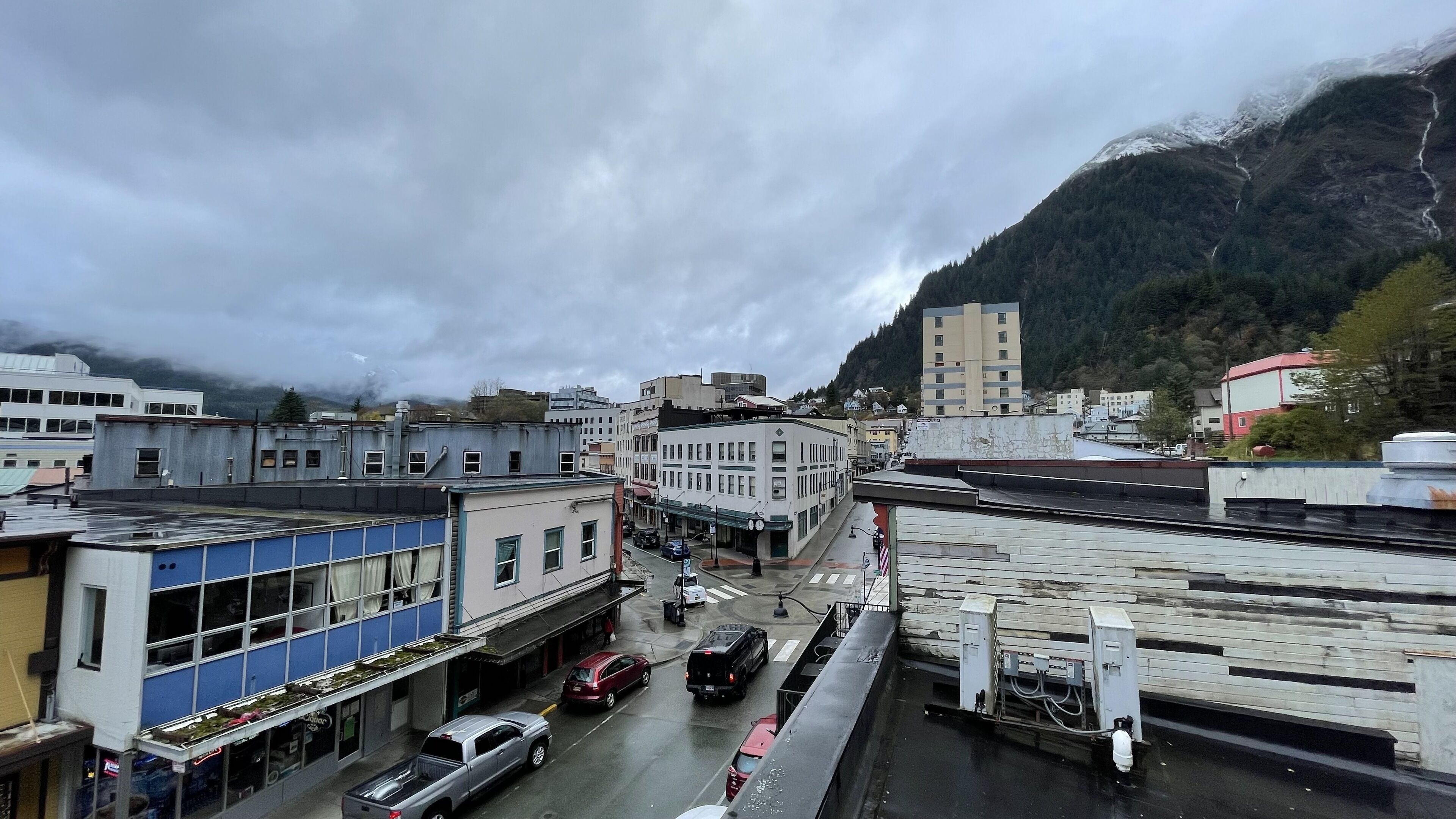 A street view with buildings, vehicles, and a mountainous backdrop.