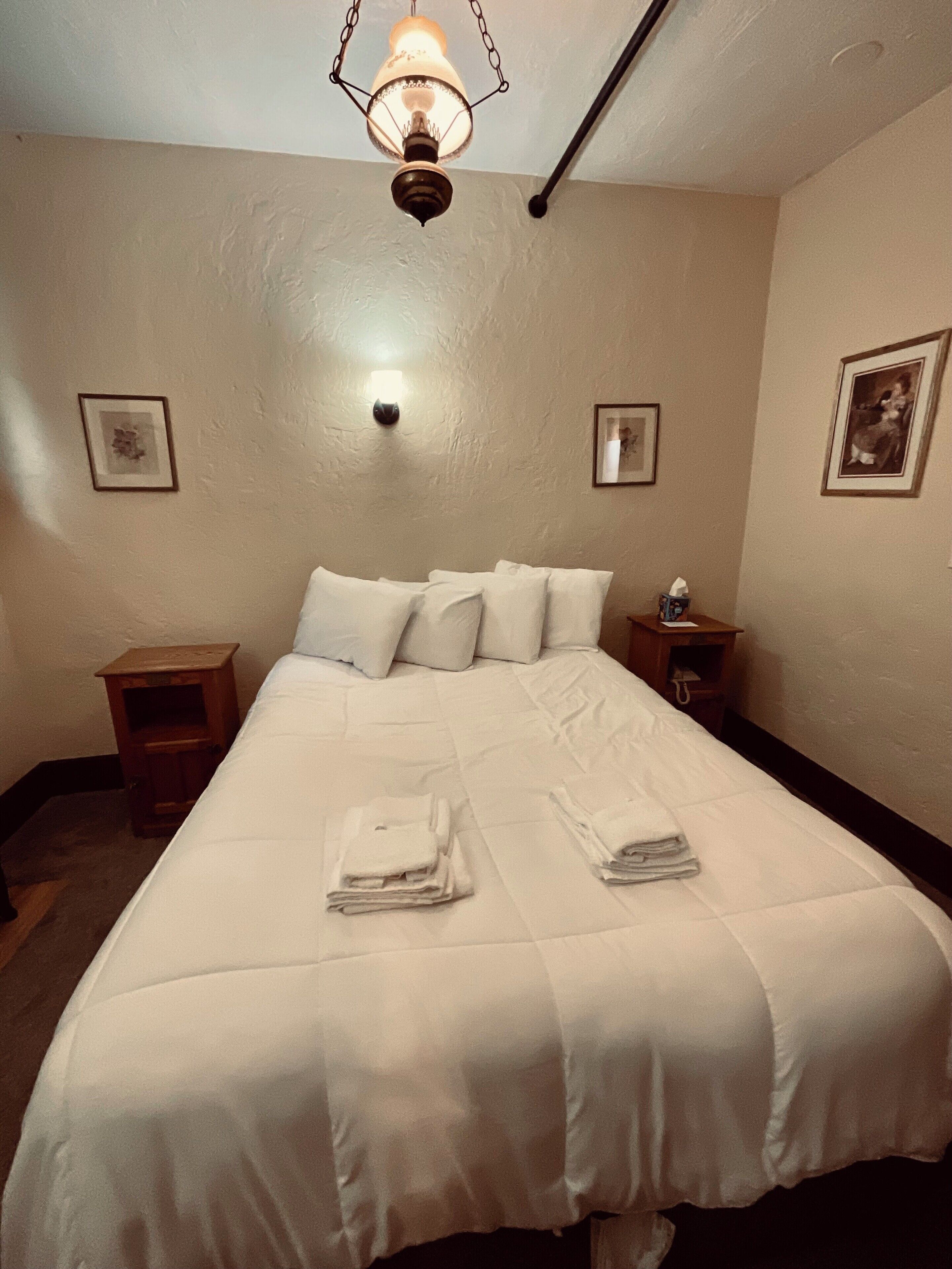 A neatly made bed with white linens, a bedside table with a lamp, and framed pictures on the walls.