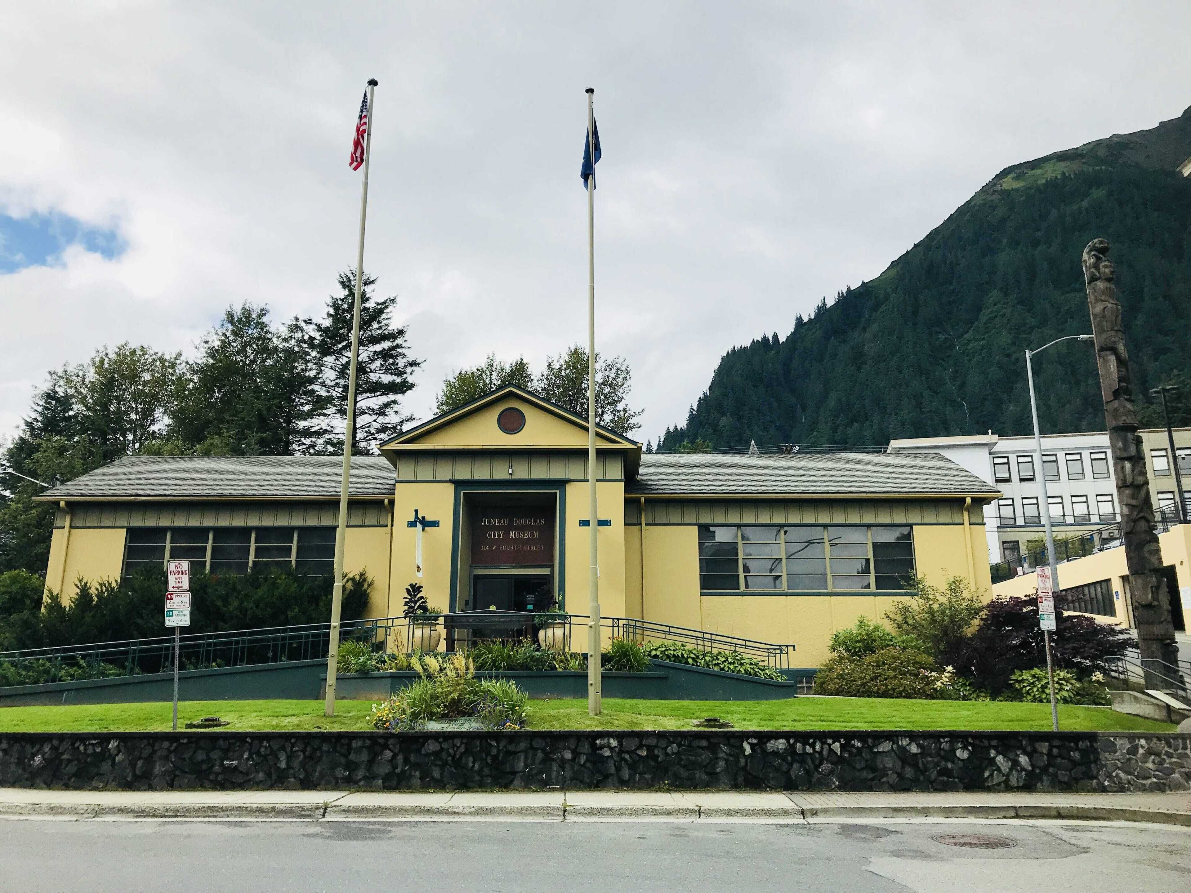 A building with a sign for the Juneau Douglas City Museum, featuring a stone wall and greenery in front.