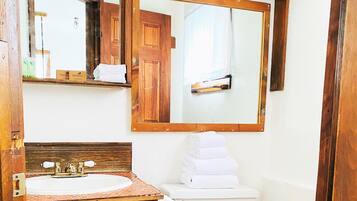 Un baño con tocador de madera, lavamanos, espejo y inodoro.