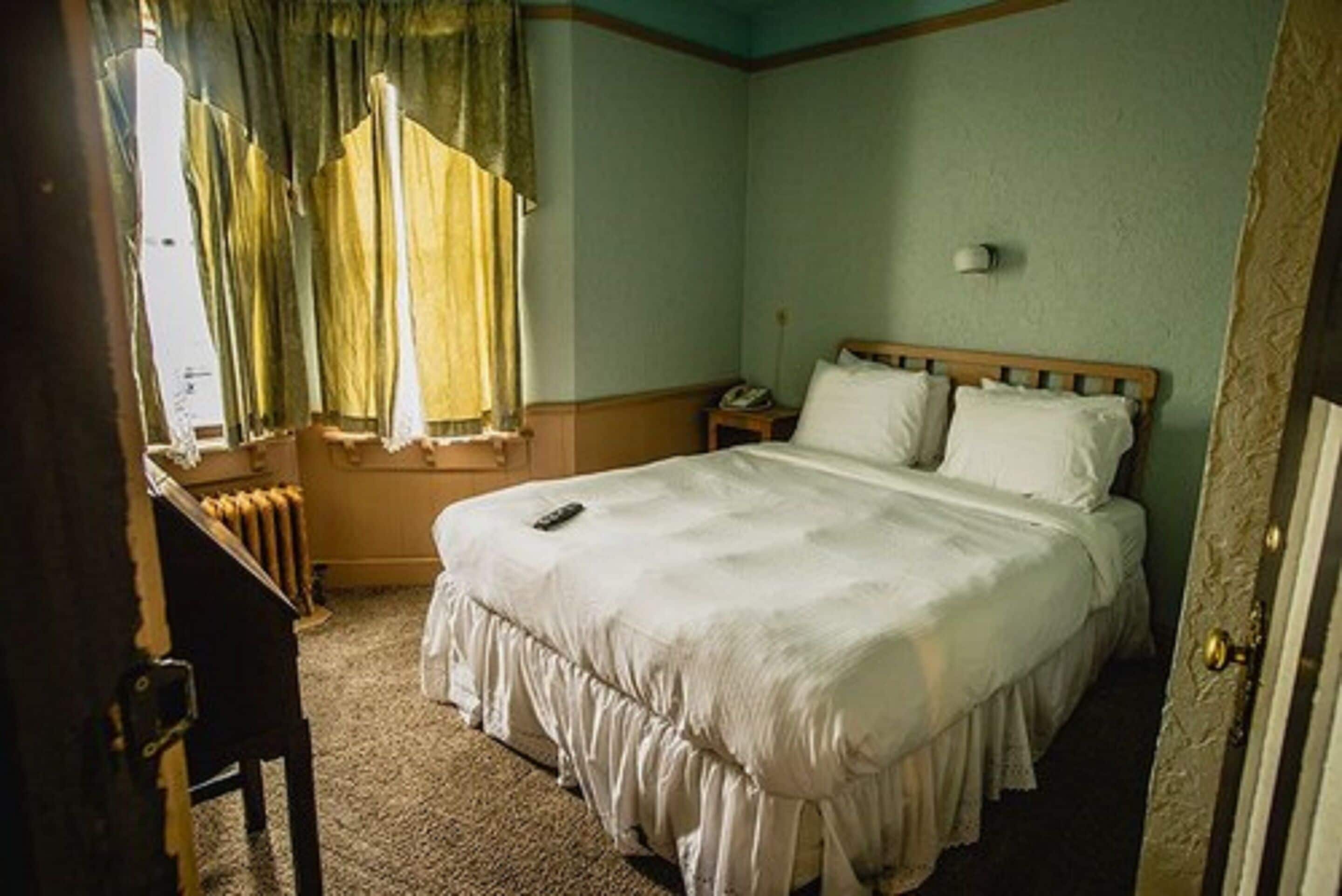 Een slaapkamer met een enkel bed, een nachtkastje, een radiator en een raam met gordijnen.