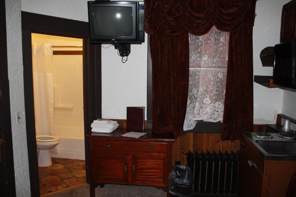Une salle de bain avec un meuble-lavabo en bois, des toilettes, un rideau de douche, un téléviseur fixé au-dessus du meuble-lavabo et un radiateur.