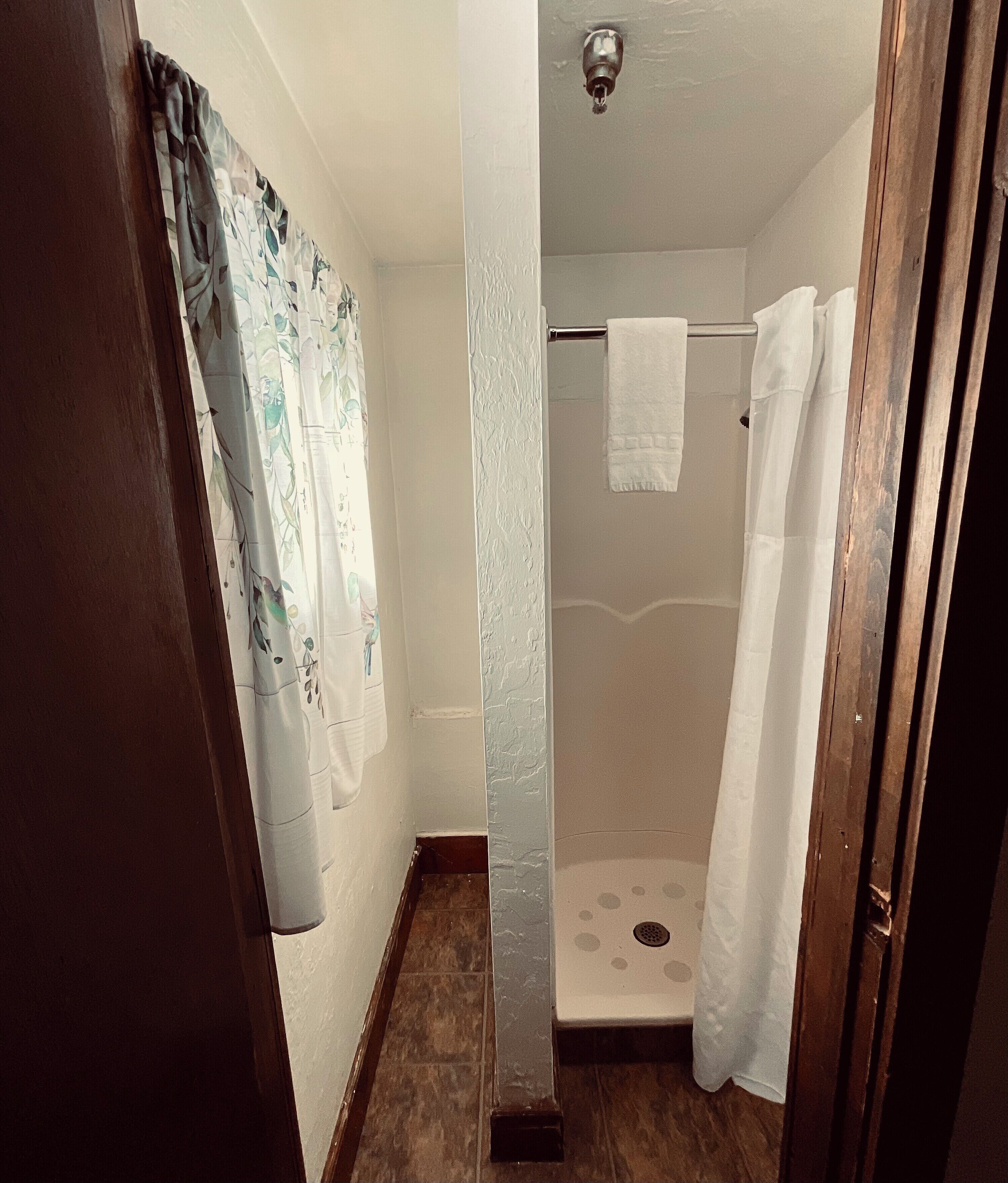 Ein schmales Badezimmer mit Dusche, einem an der Wand hängenden Handtuch und einem Holztürrahmen.