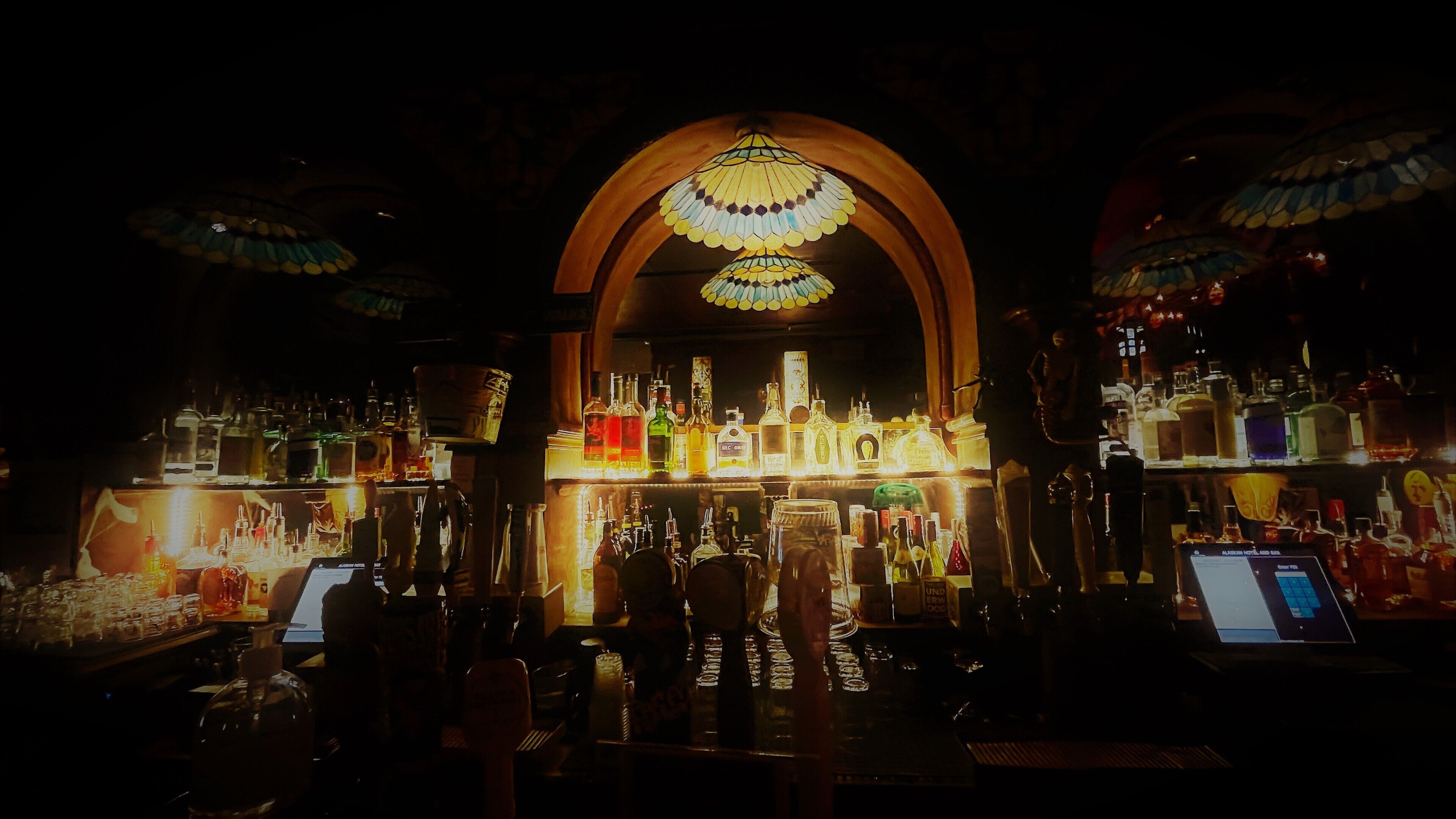 A bar with a variety of liquor bottles and a laptop on the counter.