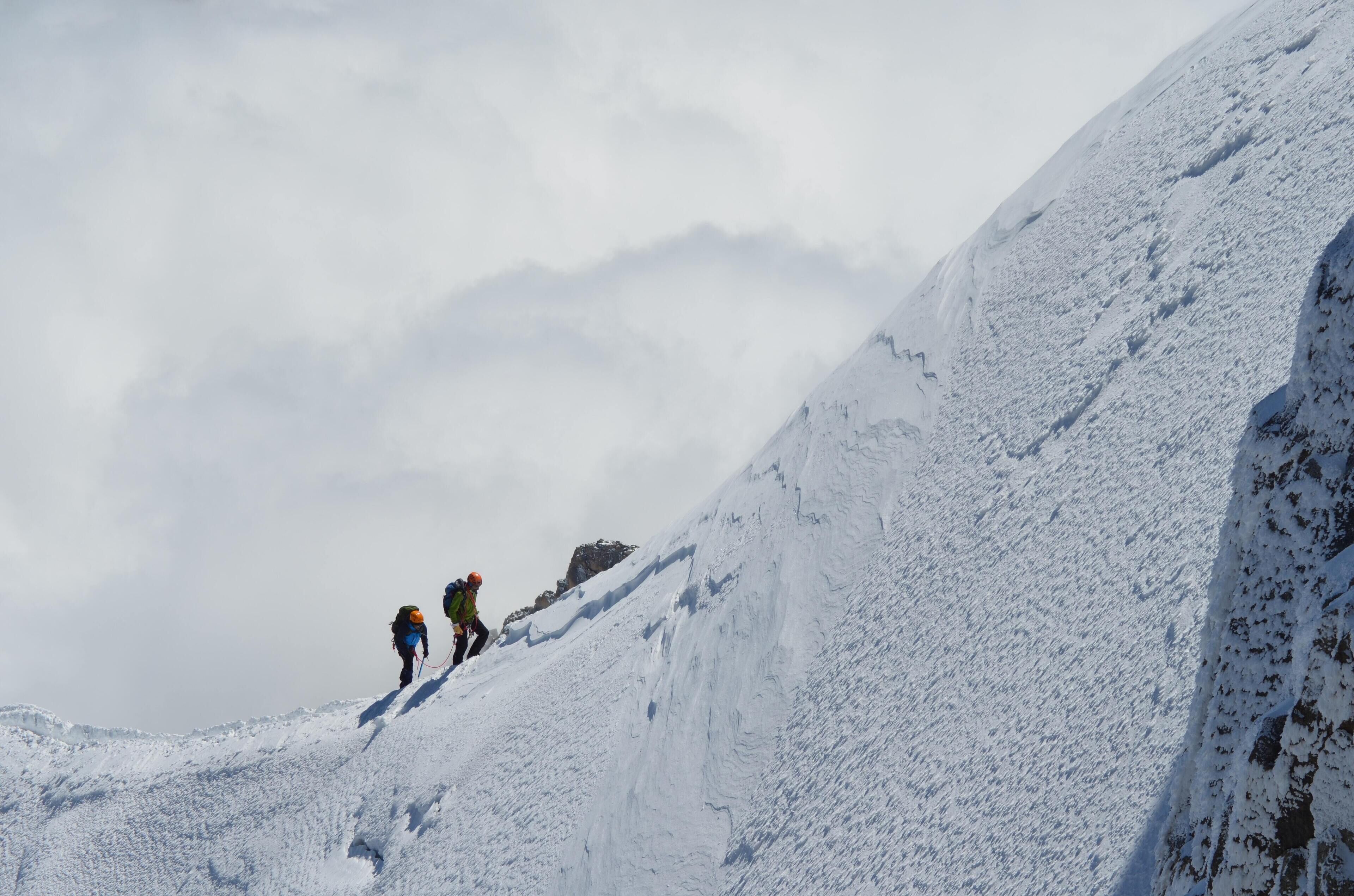 A snowy mountain slope with two hikers.