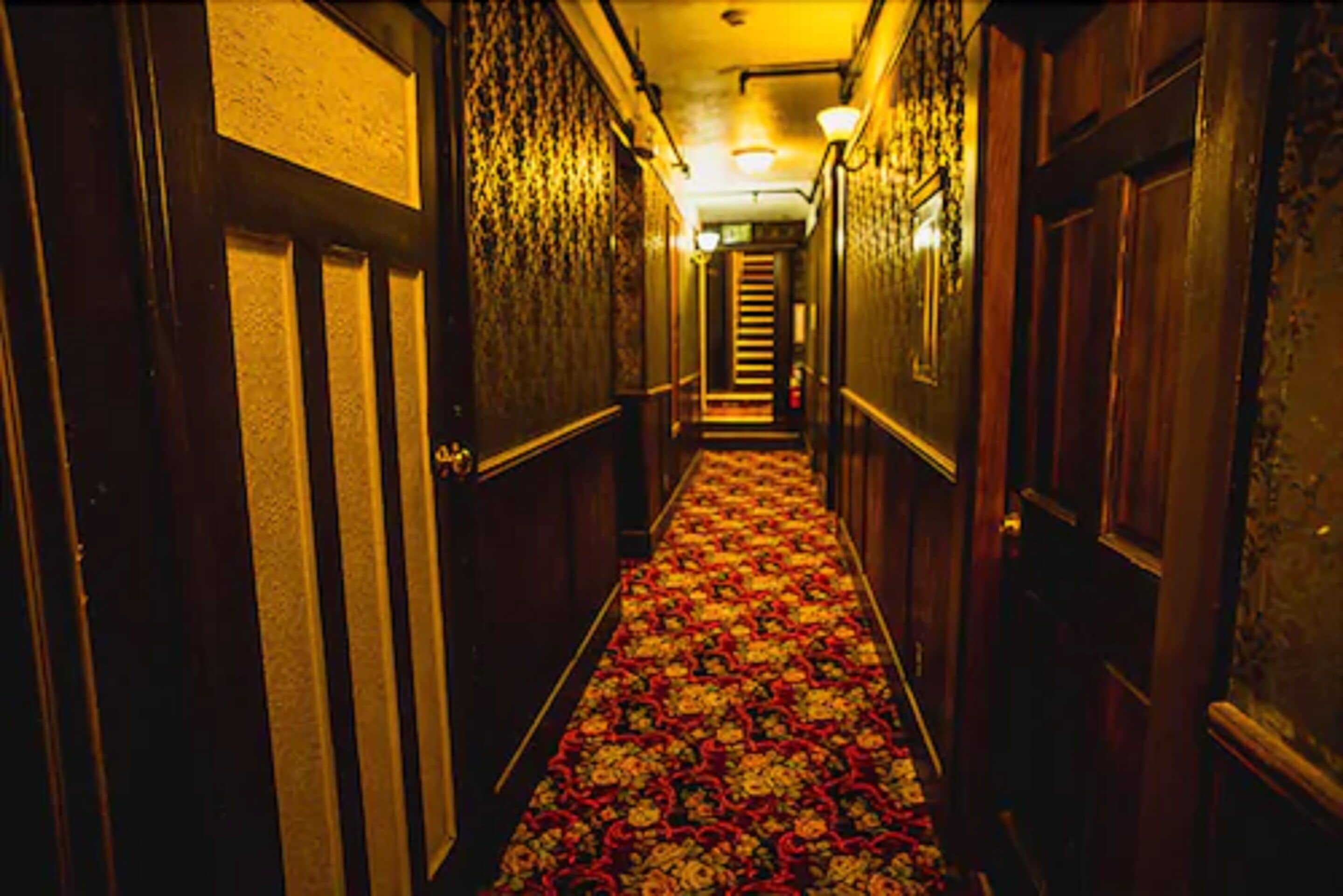 Un couloir étroit avec des portes en bois et un tapis à motifs.