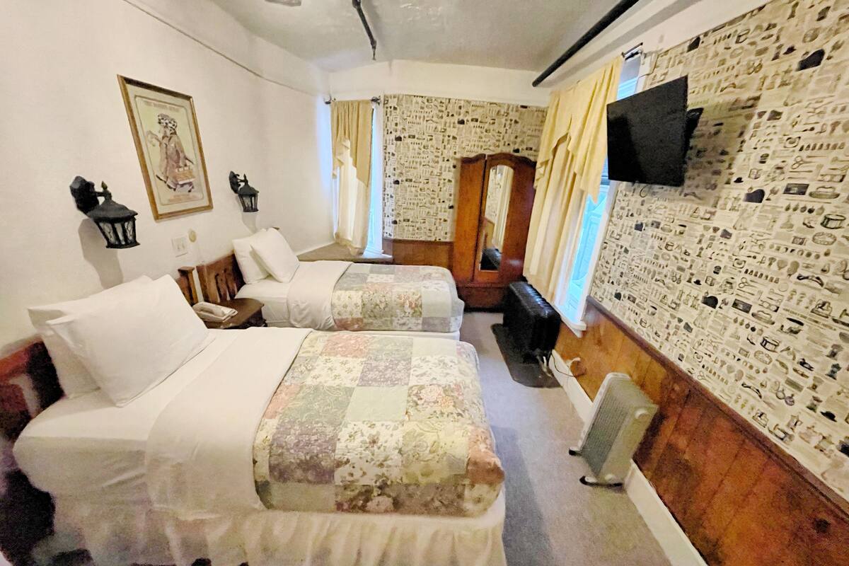 A hotel room with two beds, a television, a mirror, and a patterned wall.
