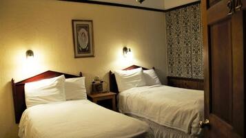 A hotel room with two beds, a nightstand with a radio, and a door with a number.