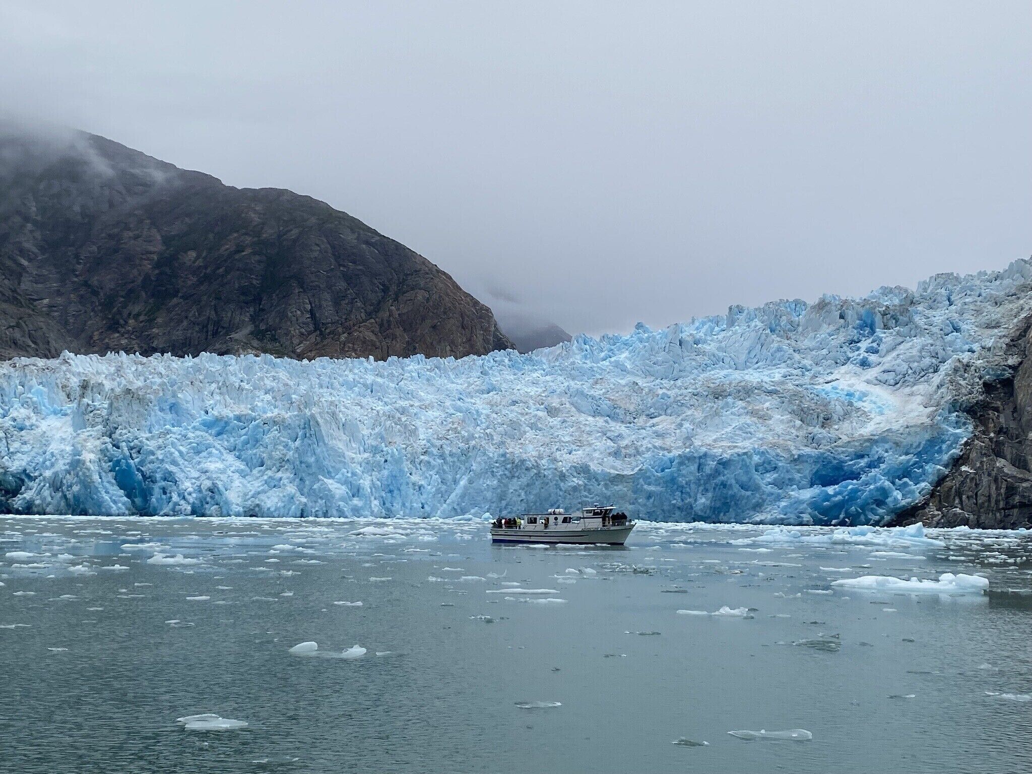 Un barco sobre un glaciar, con icebergs y montañas al fondo.