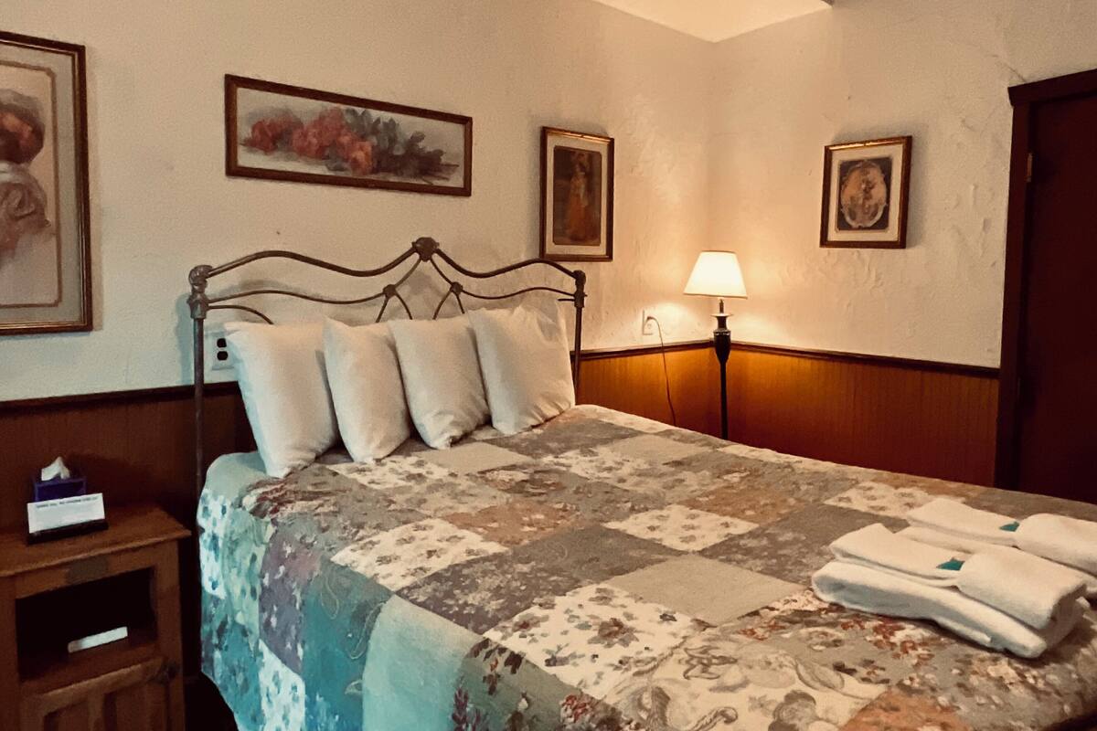 A neatly made bed with a floral quilt, a bedside lamp, and a small bedside table with a tissue box.