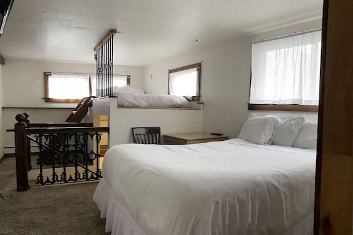 A bedroom with a bed, a chair, a desk, and a staircase.