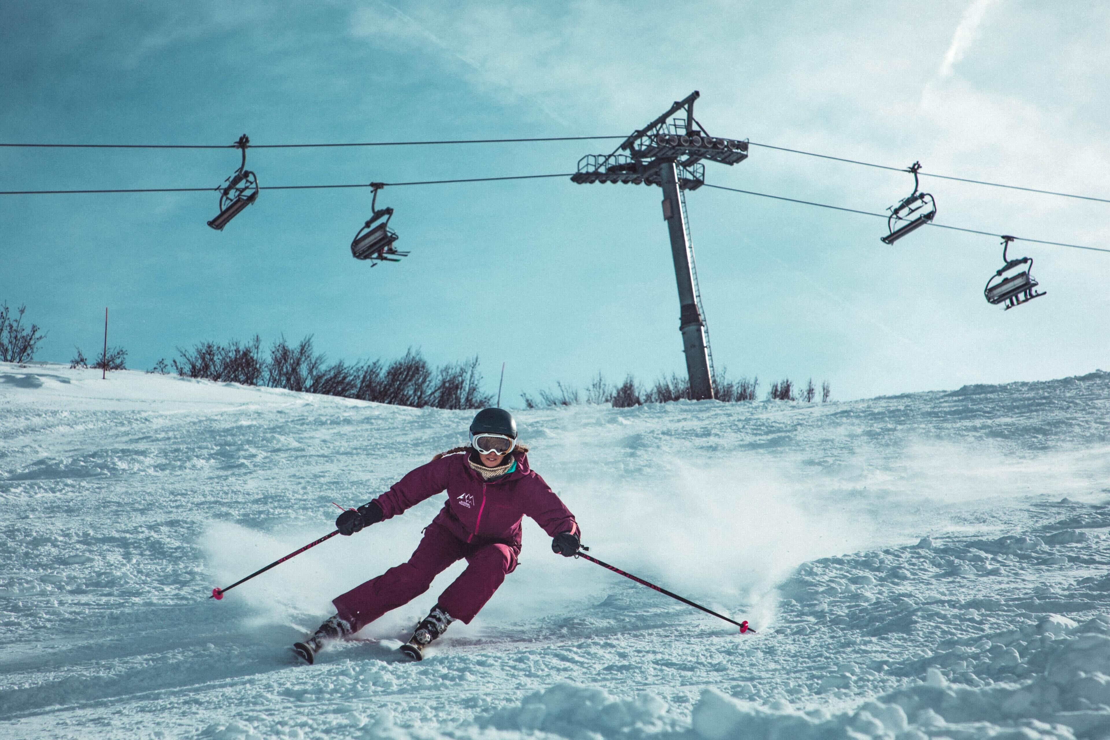 A person skiing down a snowy slope with a ski lift in the background.