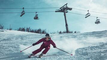 A person skiing down a snowy slope with a ski lift in the background.
