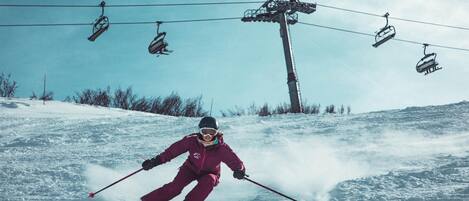 A person skiing down a snowy slope with a ski lift in the background.