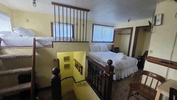 A dormitory room with two beds, a staircase, a desk, and a chair.