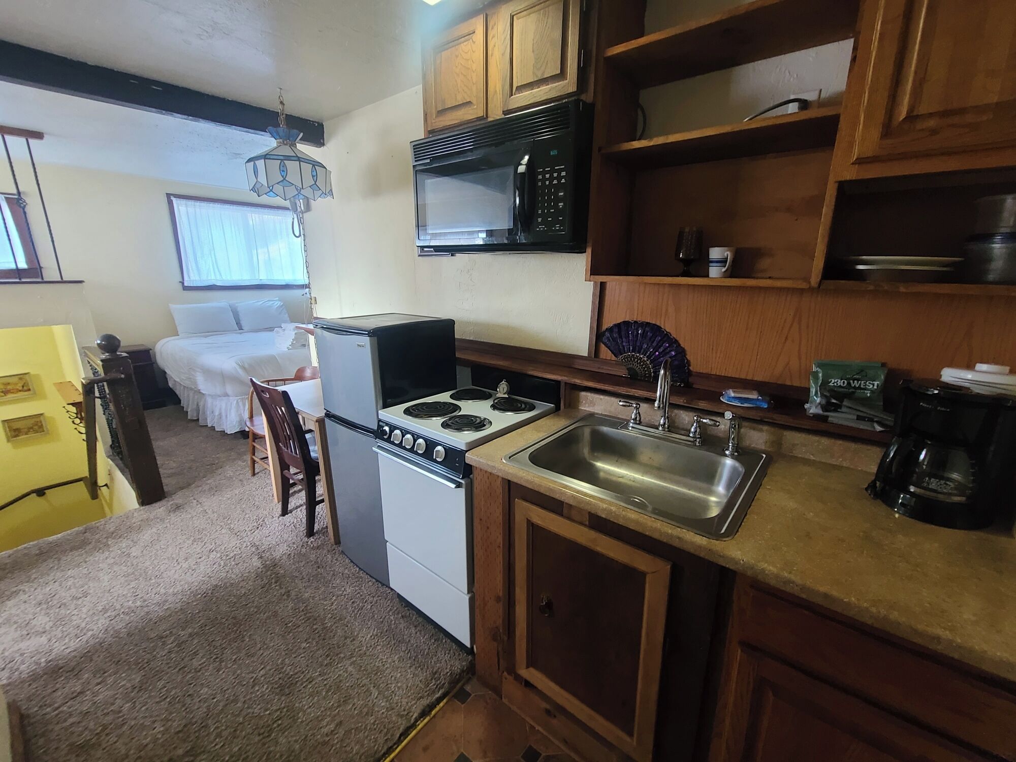 Cocina compacta con refrigerador, estufa, microondas y pileta. En la habitación contigua hay una cama.