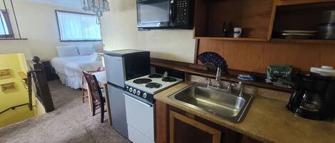 Cocina compacta con refrigerador, estufa, microondas y pileta. En la habitación contigua hay una cama.