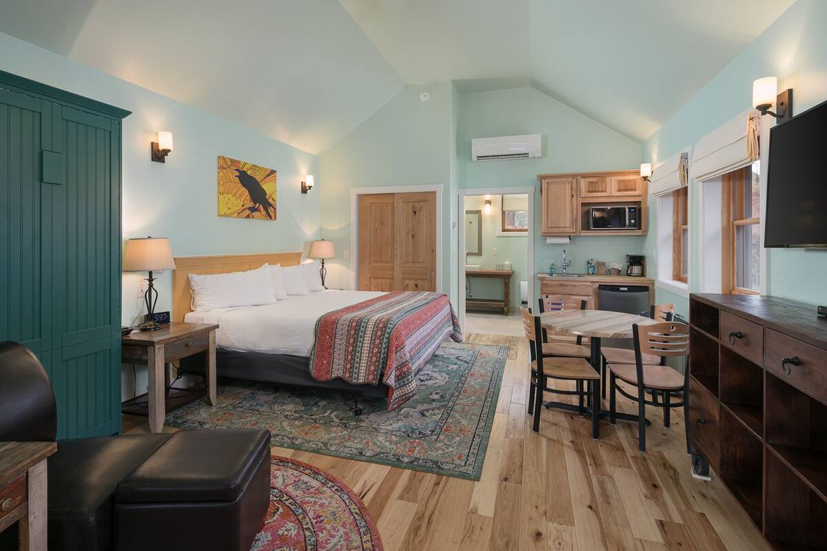 A bedroom with a large bed, a desk, and a chair, a kitchenette with a microwave and sink, and a bathroom with a shower and toilet.