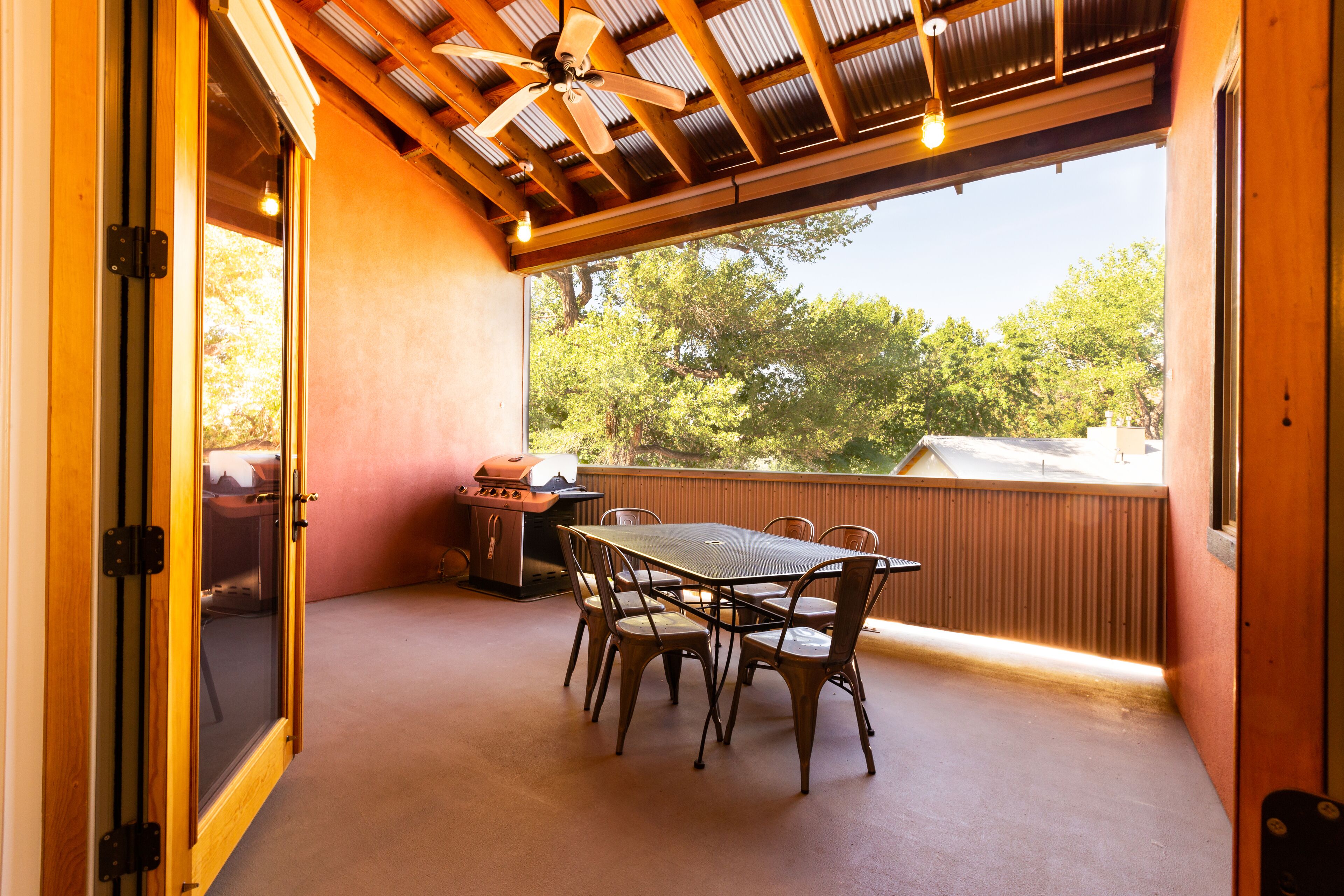 An outdoor patio with a table and chairs, a ceiling fan, and a view of trees.