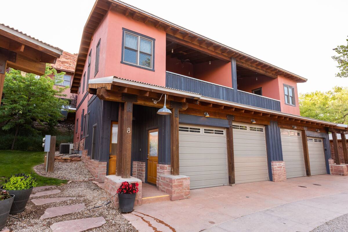 A two-story house with a balcony, a garage with three doors, and a stone pathway leading to the entrance.