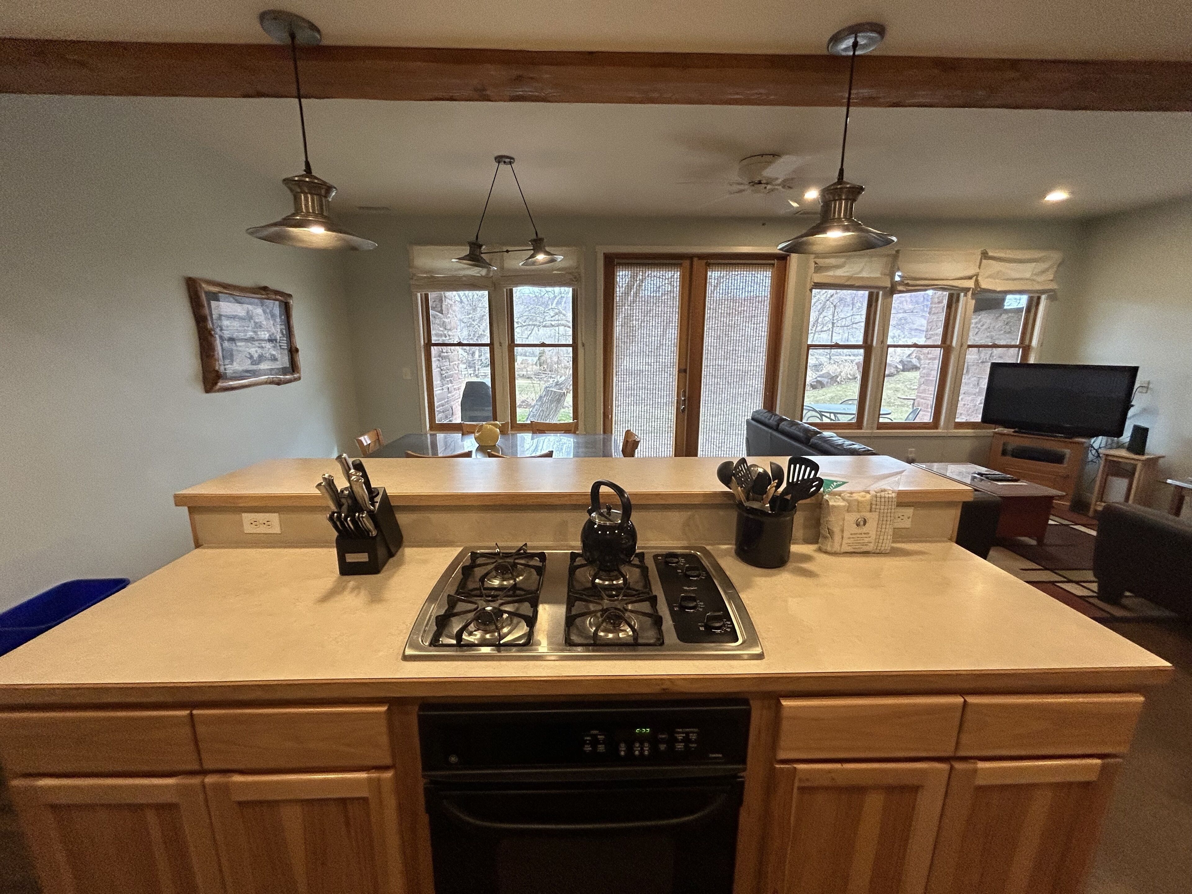 A kitchen with a gas stove, a dishwasher, and wooden cabinets. There are two hanging pendant lights and a window with blinds.