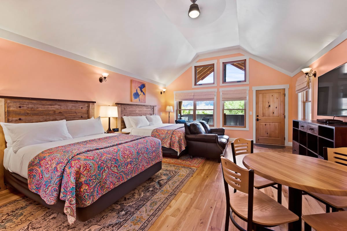 A bedroom with two beds, a dining table, and a kitchen area.