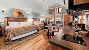 A bedroom with a large bed, a sitting area with chairs, a dining table, and a kitchen area with a stove. - Moab Springs Ranch (Moab)