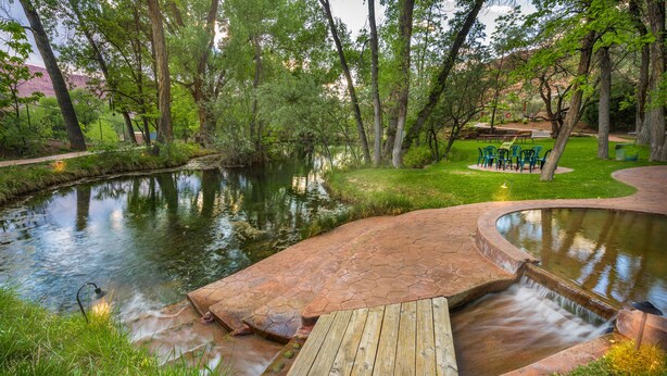 A serene outdoor area with a pond, wooden deck, and green chairs. - Moab Springs Ranch (Moab)