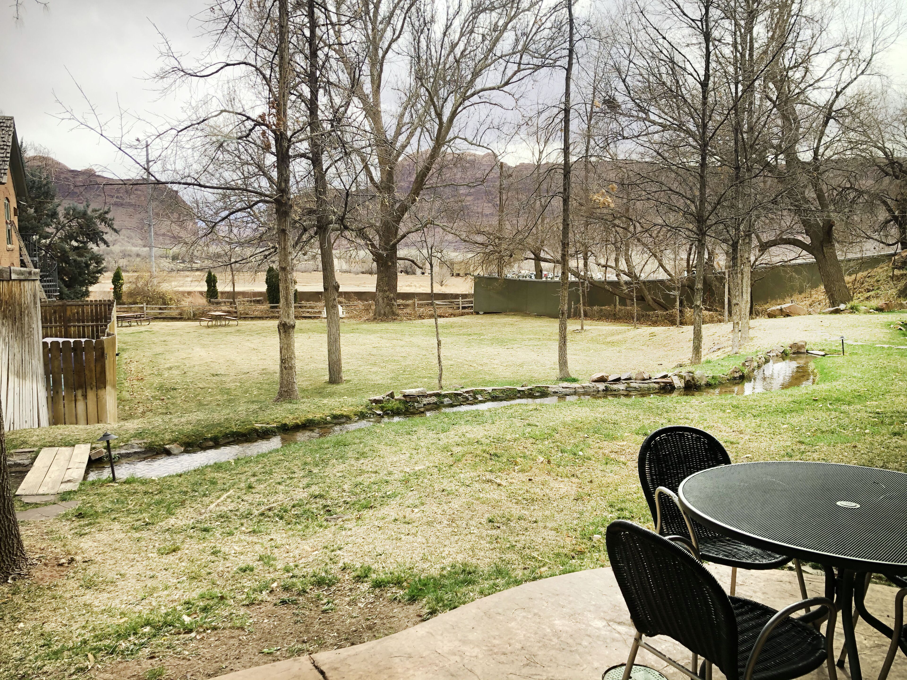 A backyard with a small stream, a wooden deck, and a table with chairs.