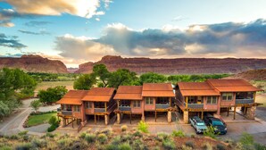 A row of rustic cabins with a mountain backdrop, featuring a central staircase and a parking area with vehicles. - Moab Springs Ranch (Moab)